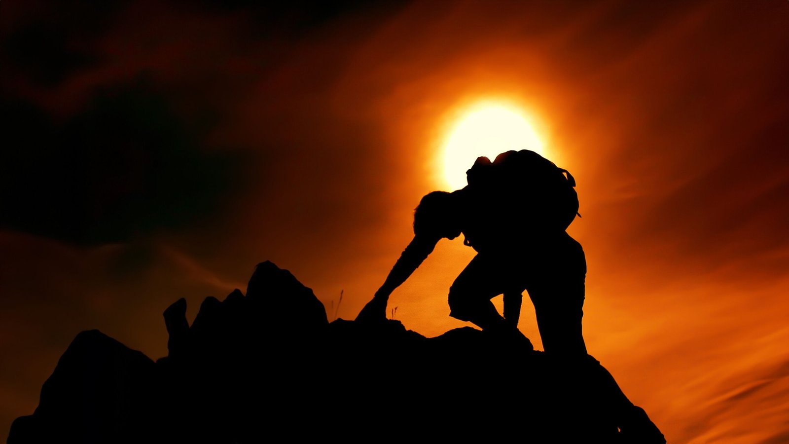 Home A silhouette of a man climbing rocks against a dramatic sunset sky, symbolizing adventure and determination.